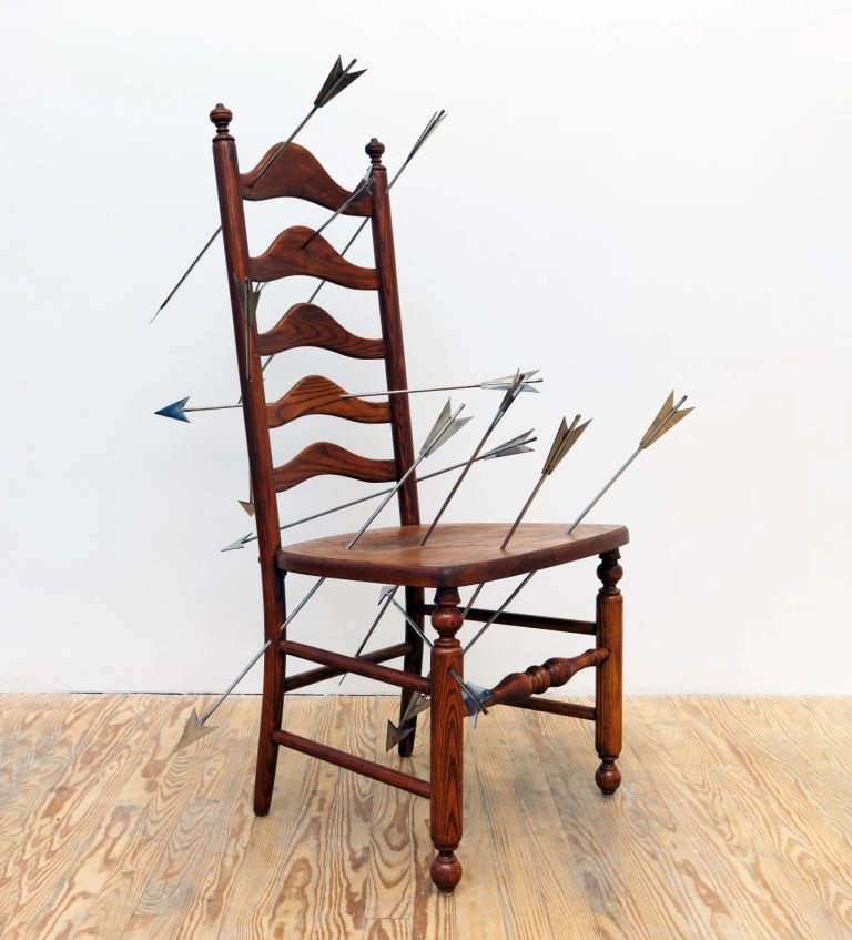 Sculpture consisting of a wooden chair with nine steel arrows piercing its seat and back