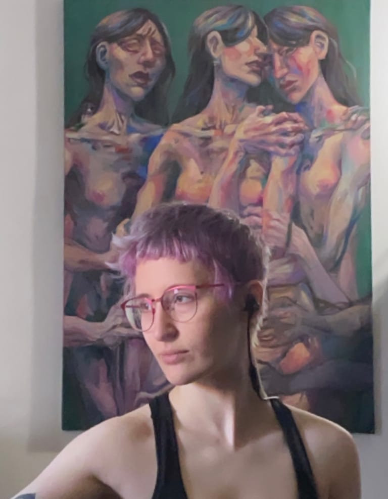 A person with short hair d light purple stands in front of a painting of three embracing nude mourning figures with long black hair