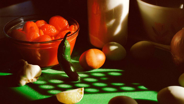 tomato from a can, jalapeño, eggs, and garlic shot on a green cutting board with light shining through a slotted spatula creating a pattern shadow on the cutting board