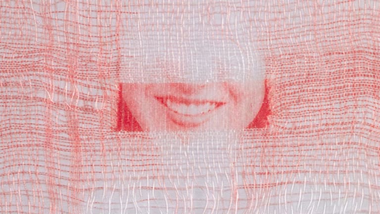 A woven photograph of a closely cropped woman's smile, made of red and white thread.