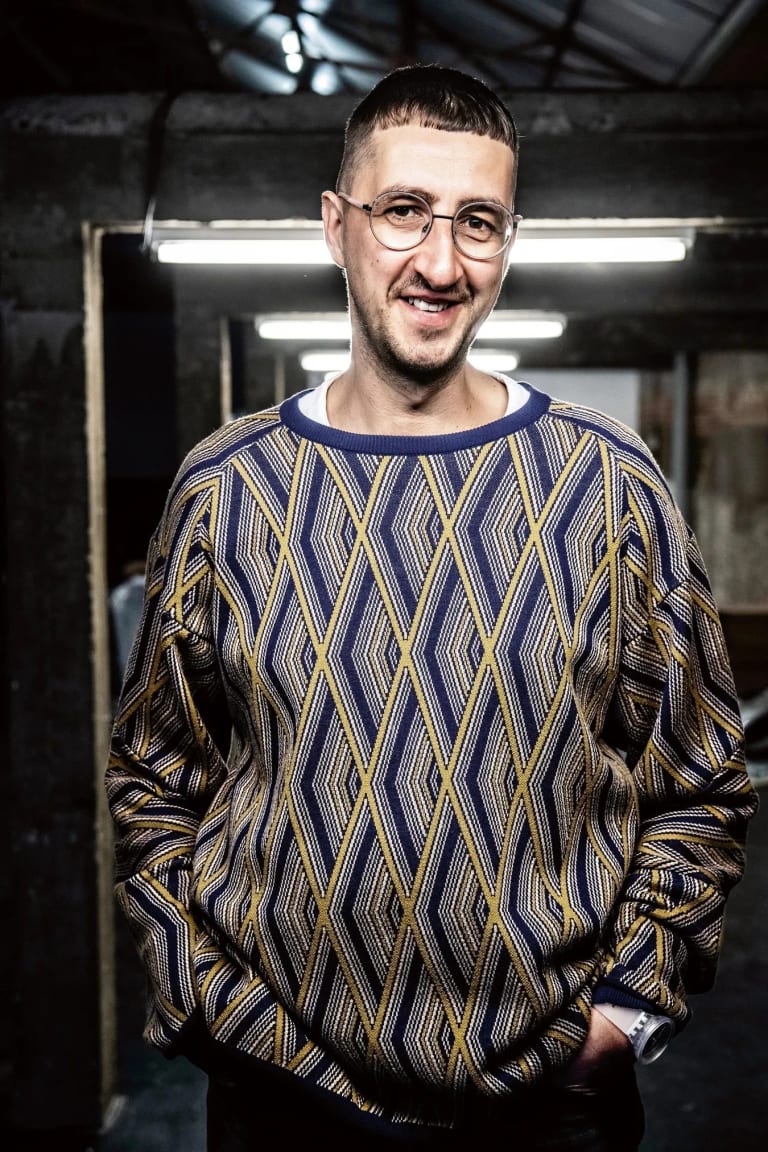 Image of Niels Van Tomme, a man in a blue and yellow diamond pattern sweater with his hands in his pockets