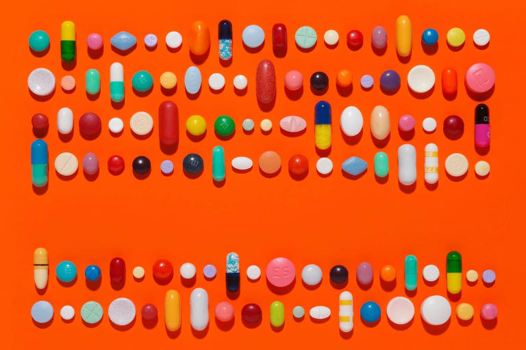 Capsules and pills in a linear composition on a bright orange background.