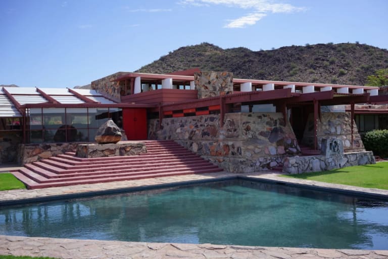 A reflecting pool in front of a modern Western ranch-style building made of brick, steel, glass, and rusticated stone, with steps leading from the building down to the pool