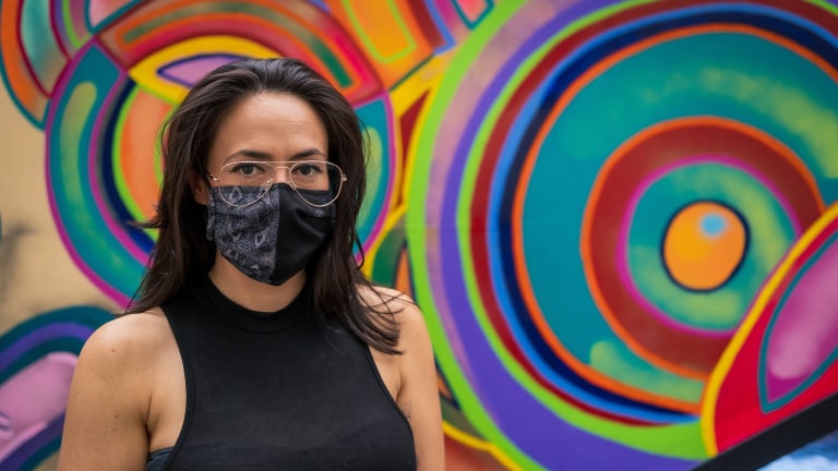 Artist Arantxa Ximena Rodríguez, wearing a mask, poses in front of her mural.