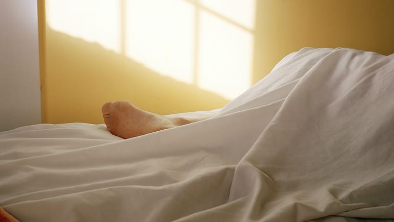 A photograph of a foot on a bed covered by a white sheet