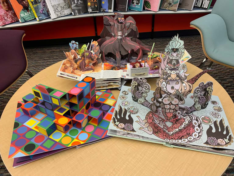 A photograph of three pop-up books opened on a table.