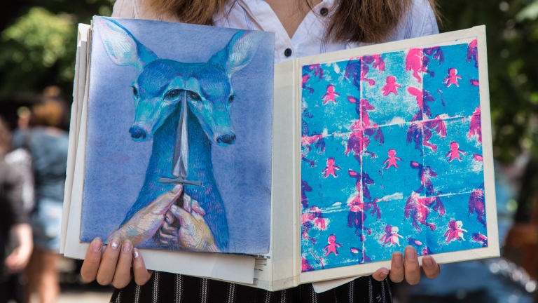 A young woman holding a sketchbook with prints and drawings