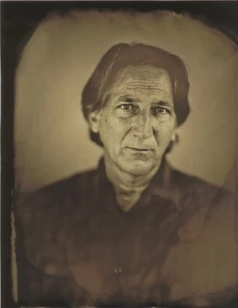 A yellow and brown toned image of a man in a black shirt looking at the camera 