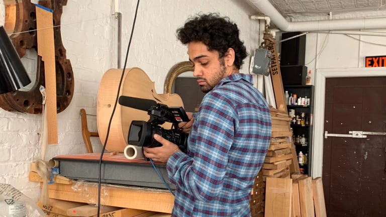 a man films, holding a video camera, in a guitar factory