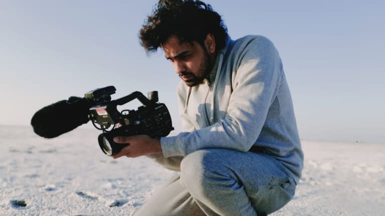a man in a grey track suit films in India's White Desert, he crouches with a focused look towards his camera