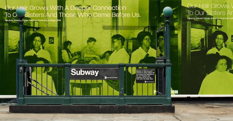 A subway station stairway with a bright green billboard in the background depicting black women caring for their hair. 