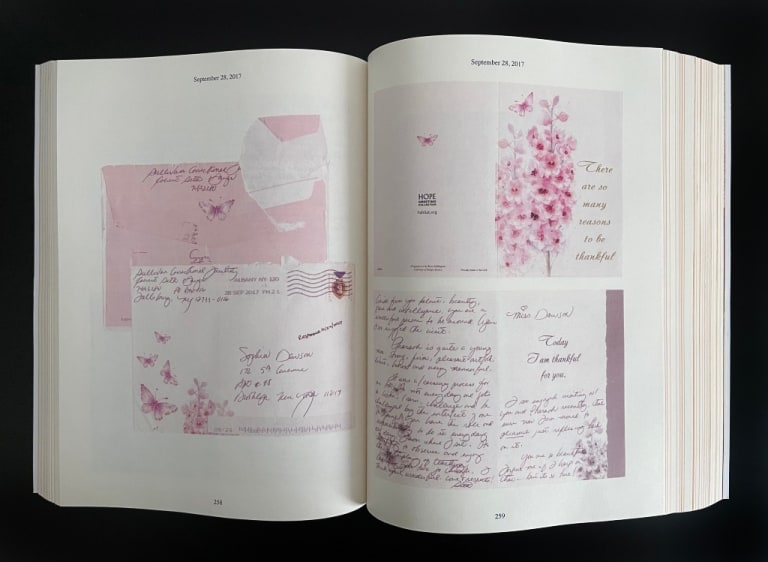 A photograph of an opened book. The pages show reproductions of a card, decorated with a printed illustration of pink flowers, and the envelope it was sent in.