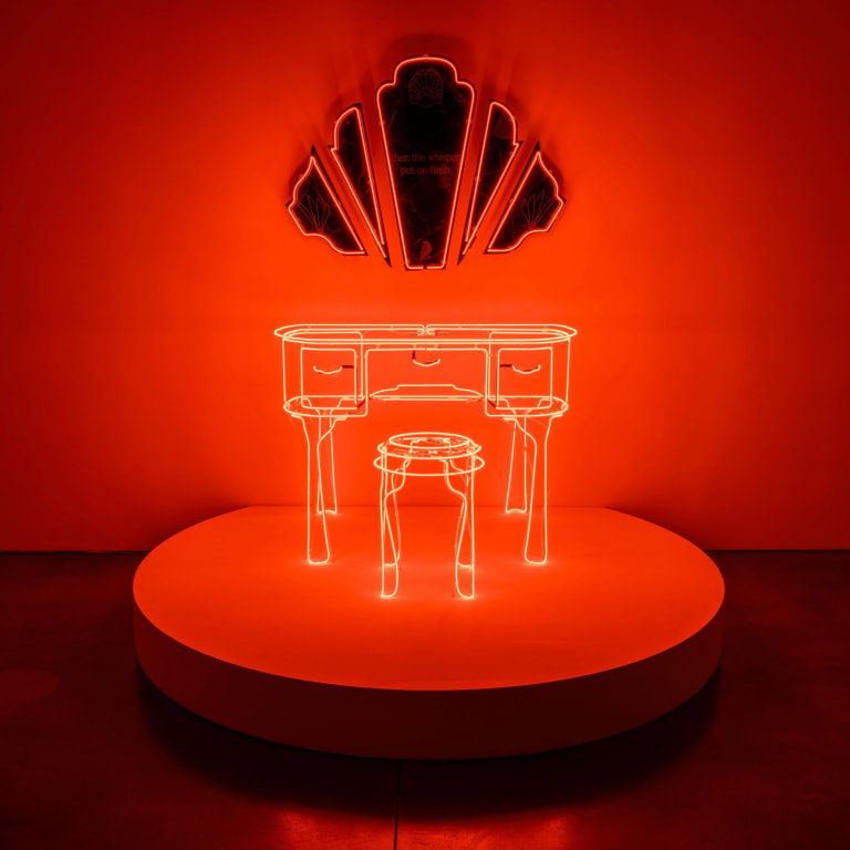 A photograph of a sculpture incorporating neon shaped into furniture forms and decorative mirrors. 