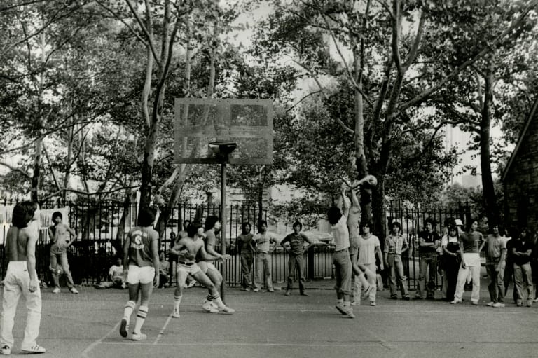 Sepia-tone B&W landscape shot image of Asian men playing basketball outside.
