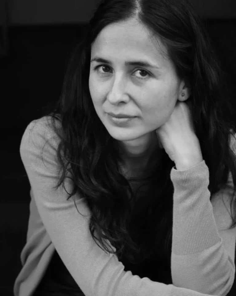 Image of a woman with her head resting on her hand in black and white. She has a light cardigan on and long dark hair.