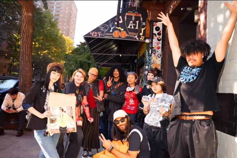 A group of students stand together pose, raise their arms and drop peace signs while smiling at the camera.