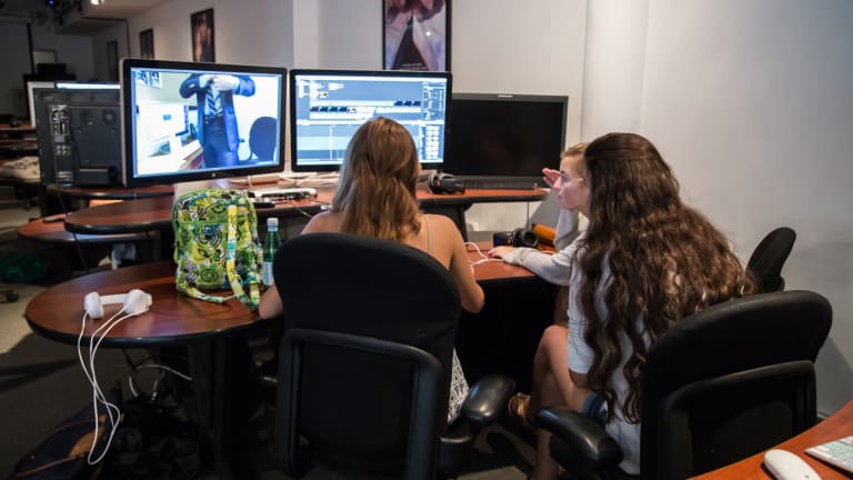 Three students sit in front of a screen looking at animation or video editing software