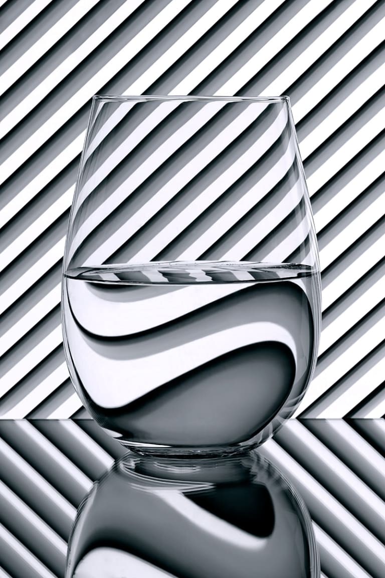 A monochrome image of what appears to be water in a glass, against a striped background.