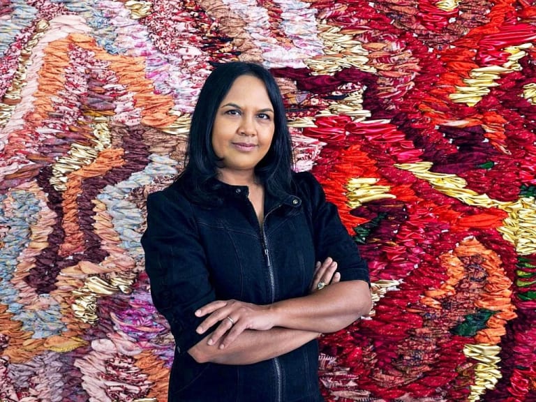 Suchitra Mattai in front of a colorful woven artwork