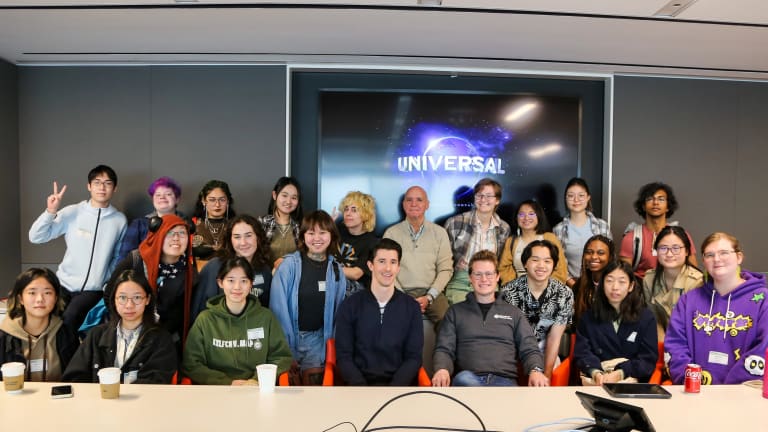 A group of students and adults, likely artists, organized in three rows and posing in front of a screen that displays Universal Studio's name and logo.