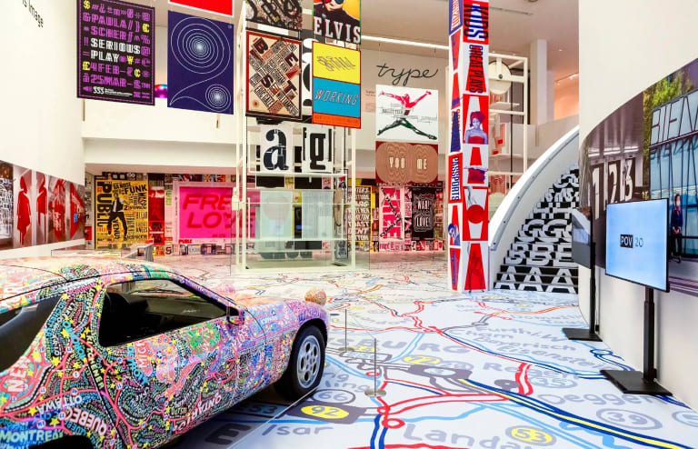 A multi-colored car parked in the middle of a colorful and dynamic looking exhibition of design and typography.