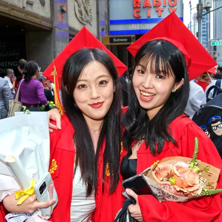 students in red caps and gowns pose outside of Radio City Music Hall for their 2024 graduation ceremony