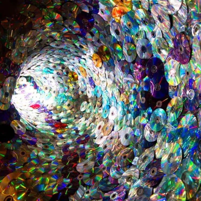 A tunnel made up of iridescent plastic CDs. A light is visible at the end of the tunnel.