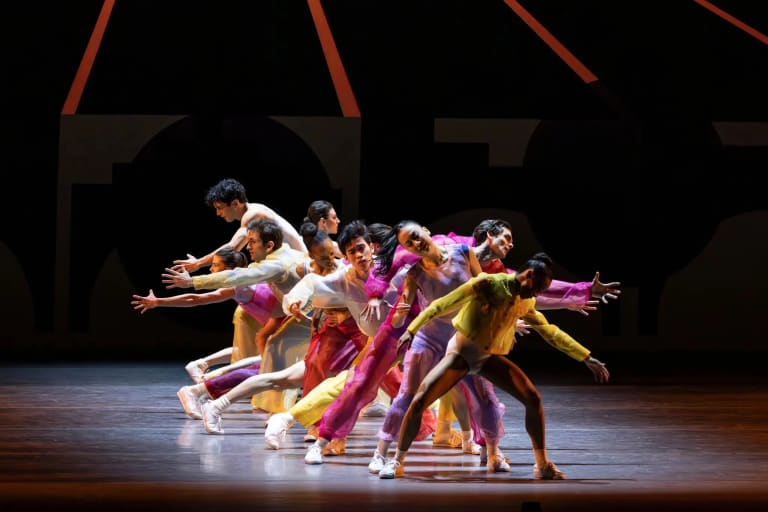 A vibrant group of dancers performing on stage, adorned in colorful outfits, showcasing their dynamic movements.