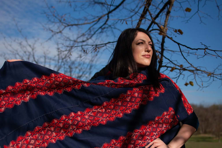 Wafa Ghnaim wearing a piece of Tatreez embroidery with red and blue colors, standing outside