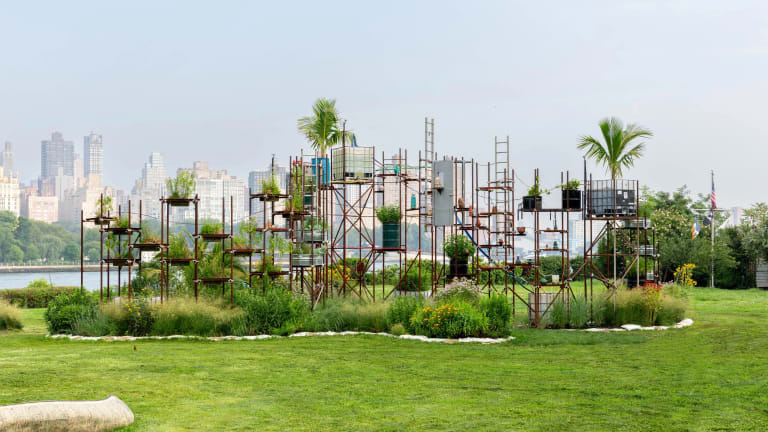 Sculpture by the artist Mary Mattingly entitled Ebb of a Spring Tide at Socrates Sculpture Park, photo Alexa Hoyer, courtesy of the artist and Robert Mann Gallery. The sculpture is a scaffold-like structure holding plants connected by an irrigation system of tubes.