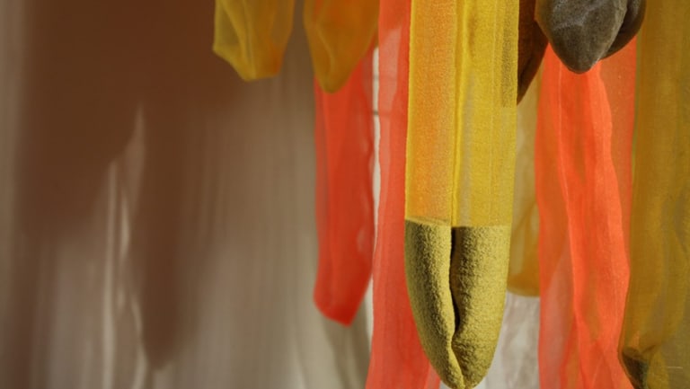 Strips and tubes of orange, yellow, and green hanging fabric against the wall