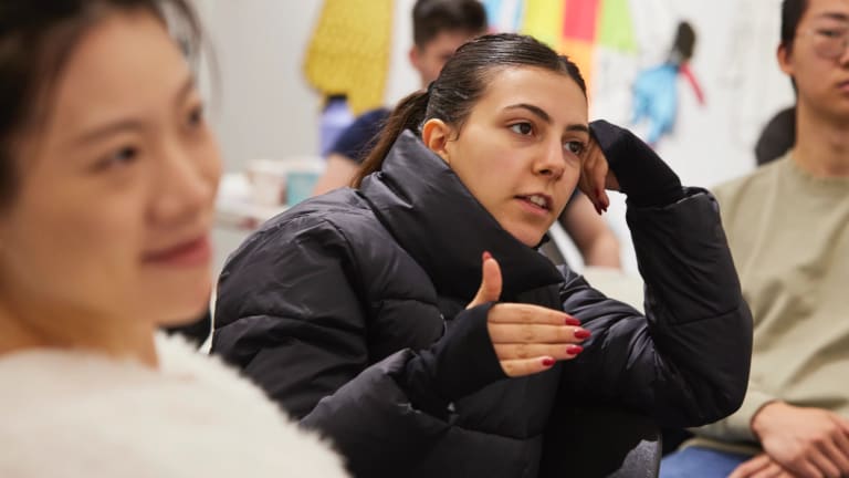 A student dressed in black making a point while students sit in the foreground and background.