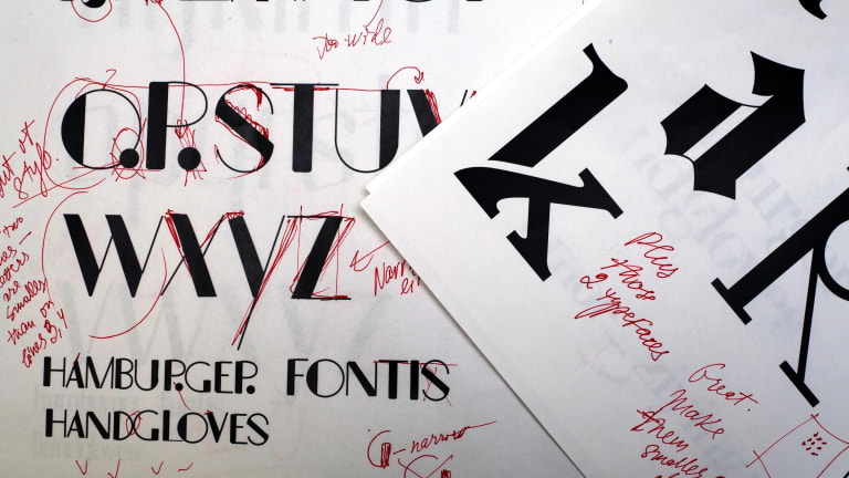 A design for a new font done on paper, scribbled up with feedback in red ink.