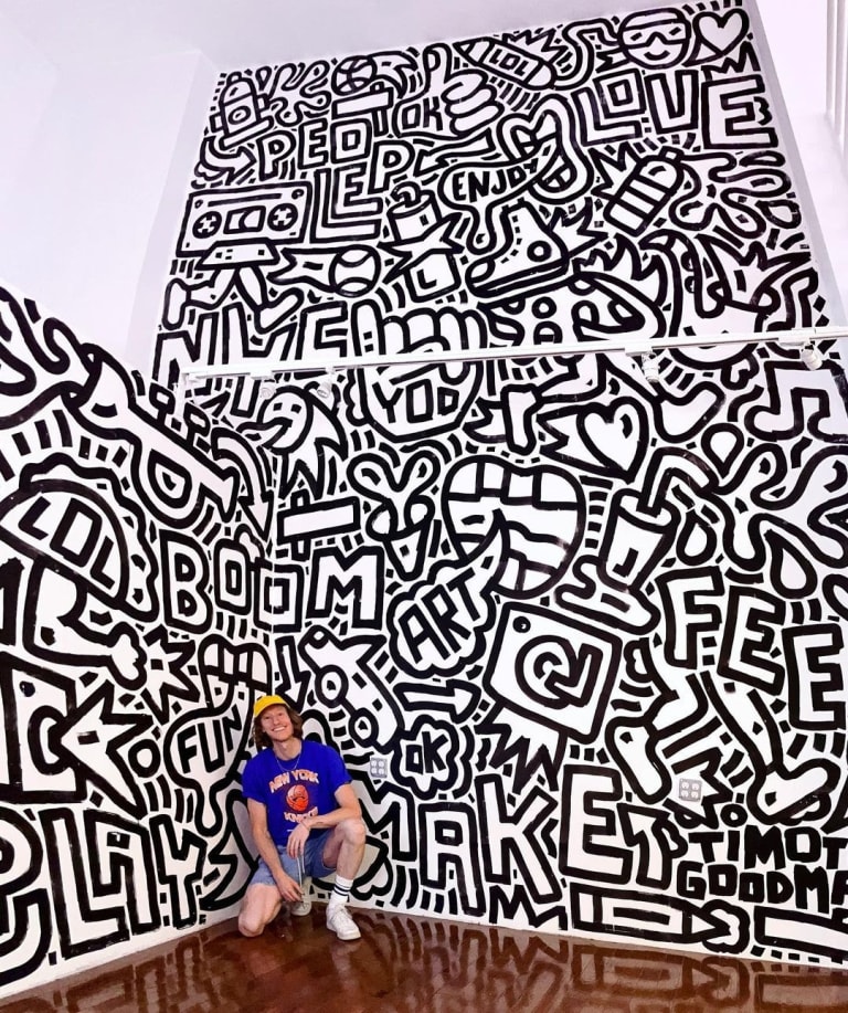 A photograph of a man posed in front of a large black-and-white mural.