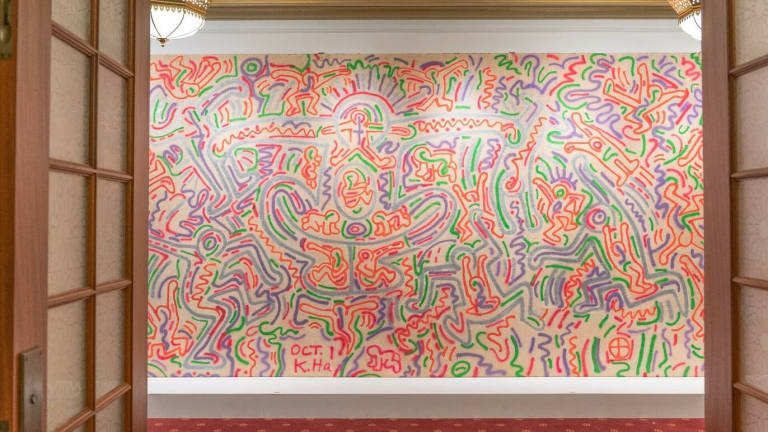 A mural by Keith Haring featuring line drawings in bright green, pink, orange and purple.