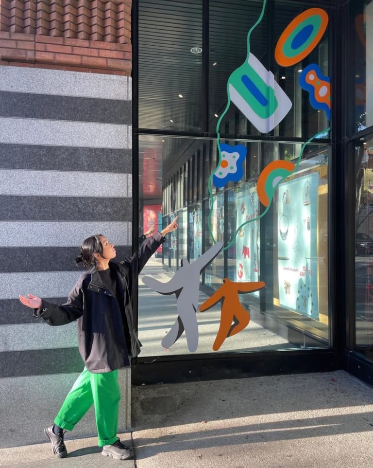 A photo of a person pointing upwards towards a window with bright, graphic illustrations on it 