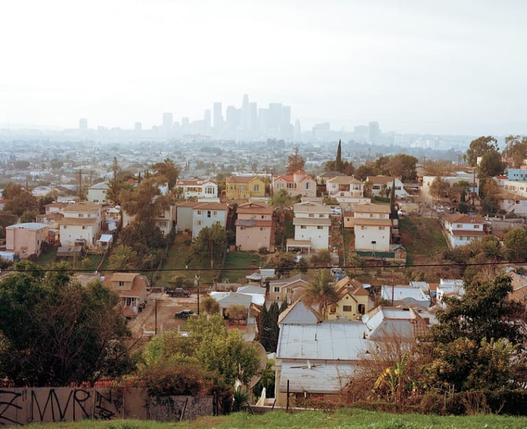 A photo of a neighborhood of houses with a cityscape in the background beyond it. The cityscape is slightly blurred by fog.