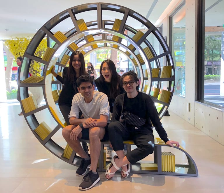 A group of young people sitting on an installation. The installation looks similar to a bookshelf and is formed in a spiral that flows away from the viewer.