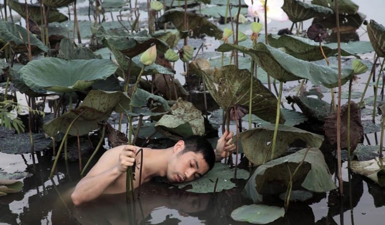 An asian person sleeping on top of a leaf in a pond.