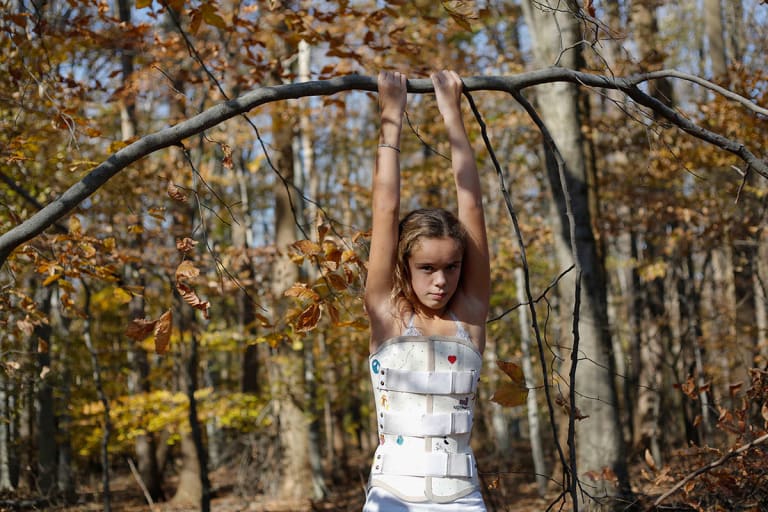 A girl in a white outfit holding onto a branch.