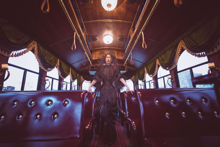 <p "="">A Victorian-style bus with a woman in all black standing in the aisle, eyes glowing white with her face covered by a black veil.
