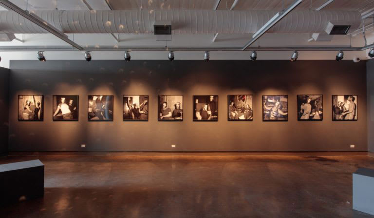 A large room with a hardwood floor and ten photographs across the back wall.