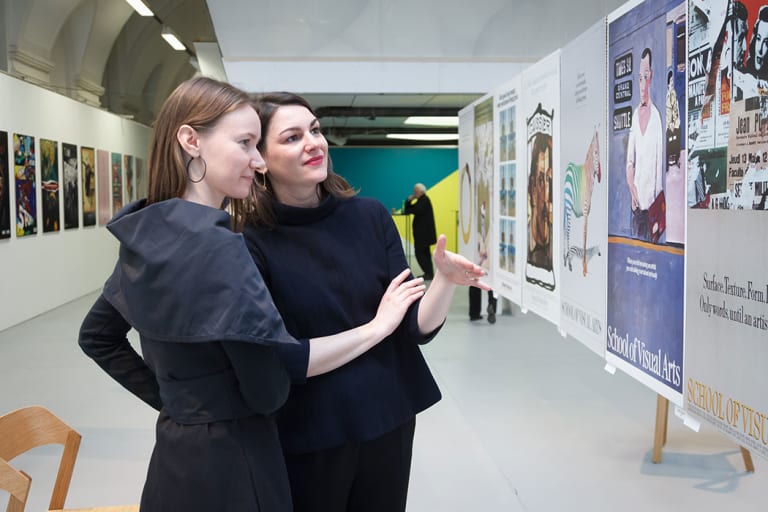 Two women discussing a poster that is hanging.