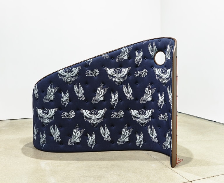 <p "="">A curving, wall-like sculpture upholstered in blue tufted denim that has been printed with several images of birds, which have been rendered in white lines.
