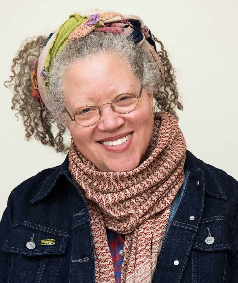 A woman wearing glasses, a scarf and denim jacket smiles.