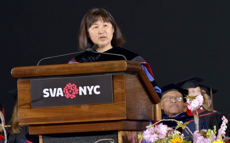A woman speaks at a podium at a graduation ceremony.