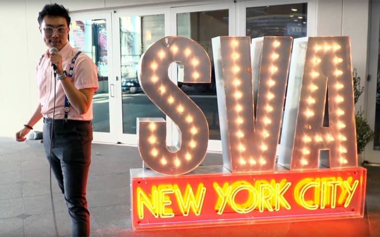 A picture of an Asian man wearing glasses next to a neon lights sign.