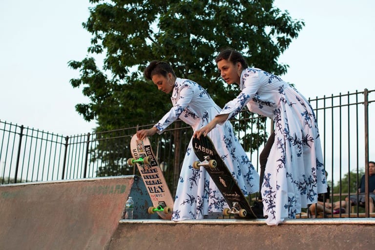 Two ladies skateboarding while wearing a dress.