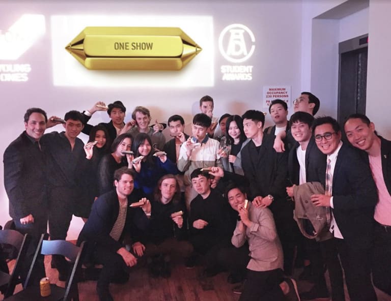 A group photo of people who have won an award. Everyone looks happy and each person is holding a gold item.