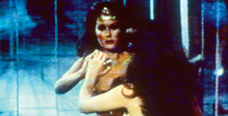 wonder woman in a physical struggle with another woman in a room with windows; its dark outside